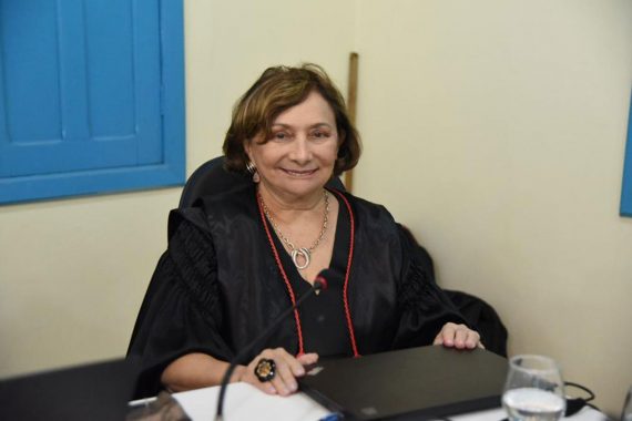 Foto da desembargadora Eva Evangelista. Ela está sentada à mesa, com um notebook à sua frente. Ela está usando toga e está no Centro Cultural do Juruá.