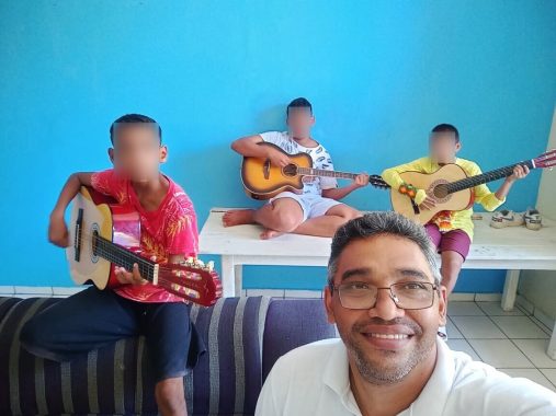 Selfie do voluntário com três crianças com violão no colo