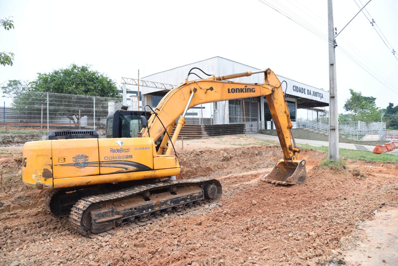 Na foto: Retroescavadeira de cor amarela, realizando obras de engenharia civil para reforma e ampliação da guarita existente na Cidade da Justiça. Ao fundo portal de entrada e saída da cidade da justiça.