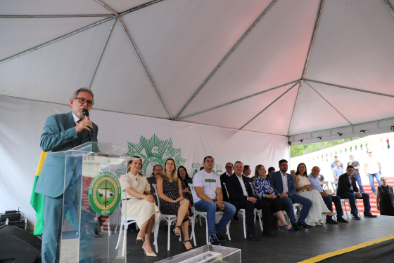 Foto do vice-presidente do TJAC, desembargador Luiz Camolez, na inauguração da carreta itinerante da DPE. Ele discursa no púlpito na solenidade de implantação da unidade móvel. O desembargador é branco, grisalho, aparente ter cerca de 50 anos e veste um paletó azul-marinho. Ao fundo, estão as demais autoridades do Estado, como o governador e o presidente da Aleac.