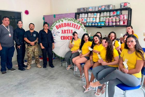 Foto do projeto Borboletas e Artes realizado na penitenciária de Tarauacá. Há 12 reeducandas sentadas do lado esquerdo mostrando a agulha de crochê, na parede há uma parede com as linhas compradas para serem usadas nas aulas, os policiais penais estão ao lado, juntamente com um representante da Comarca.