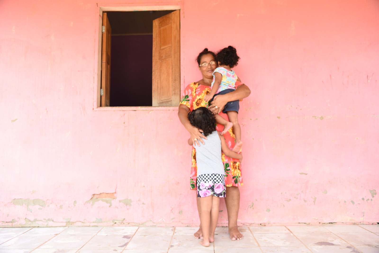 Fotografia feita em uma casa, localizada na cidade de Rio Branco, Estado do Acre, onde mostra família beneficiada com o programa “Família Acolhedora”. TJAC fortalece programa social voltado para crianças e adolescentes Ser família acolhedora é cuidar, dar colo, proteção e muito carinho em um momento de vida fundamental para uma criança ou adolescente que precisou ser afastado de sua família de origem O programa “Família Acolhedora” é um programa desenvolvido pela Prefeitura de Rio Branco (PMRB), por meio da Secretaria Municipal de Assistência Social e Direitos Humanos (SASDH), em parceria com o Tribunal de Justiça do Acre (TJAC). O intuito é abrigar voluntariamente, por período provisório, crianças e adolescentes por até 18 meses. Em Rio Branco, é oferecida uma bolsa-auxílio de um salário mínimo, para os cuidados necessários do infante. O coordenador do serviço de acolhimento familiar da PMRB, Crispim Machado, destaca que o programa até o momento tem nove crianças e adolescentes em situação de risco e vulnerabilidade sob cuidados de outras famílias. “Quando a família acolhedora é bem capacitada e cadastrada no sistema de acolhimento, a probabilidade da criança ou adolescente retornar a sua família de origem é muito grande,” conclui. Todo esse empenho pode ter ainda mais resultados, desde que mais pessoas ajudem. Não há restrições de gênero, raça ou orientação sexual, pois é preciso apenas o desejo de cuidar, dar carinho e ter disponibilidade para atender temporariamente a criança ou adolescente. Para a secretária do lar, Romilda Guimarães, que tem um filho biológico e ainda acolhe duas crianças, ela destaca que conheceu o programa dentro da igreja onde frequenta e elogia o fato de poder dar um lar e amor para as meninas. “Temos a oportunidade de conhecer as crianças, de dar amor e carinho como se fosse da gente, além de auxiliar na alimentação e na compra de produtos de bem-estar e higiene.” Romilda comenta ainda sobre o acompanhamento técnico e faz um chamado para as pessoas interessadas, “Nós recebemos sempre a orientação e visita da Assistência Social. Faço um convite para todas as famílias interessadas ou que tiverem interesse em participar. Que Deus abençoe mais famílias para cuidar dessas crianças. Enquanto tiver saúde e forças, vou continuar acolhendo crianças,” finaliza Guimarães. Família Acolhedora O programa Família Acolhedora seleciona famílias e indivíduos e fornece capacitação para receber, em suas residências, até duas crianças, em regime de guarda provisória. O trabalho tem a missão de propiciar que crianças e adolescentes, em situação de vulnerabilidade, sejam recebidas em um lar e não direcionadas para instituições. Assim, essas crianças ou adolescentes ficam provisoriamente com famílias acolhedoras pelo período que se busca a reintegração na família biológica. As condições são: ser maior de 21 anos, não ter antecedentes criminais, residir em Rio Branco e não estar inscrito no cadastro de adoção nas varas especializadas da infância e juventude. Dúvidas sobre o Programa Família Acolhedora? Ligue (68) 99946-5457 e descubra se você está pronto para dar e receber amor incondicionalmente, mesmo que por algum tempo. Os participantes precisam estar sempre cientes de que o serviço de acolhimento familiar é, por natureza, provisório, uma vez que a qualquer momento a criança ou adolescente acolhido pode ser reinserido na família de origem, se houver a possibilidade. Portanto, ao entrar para o programa o participante deve saber que os laços afetivos devem ser construídos com base na devolução futura do menor ao núcleo familiar biológico.