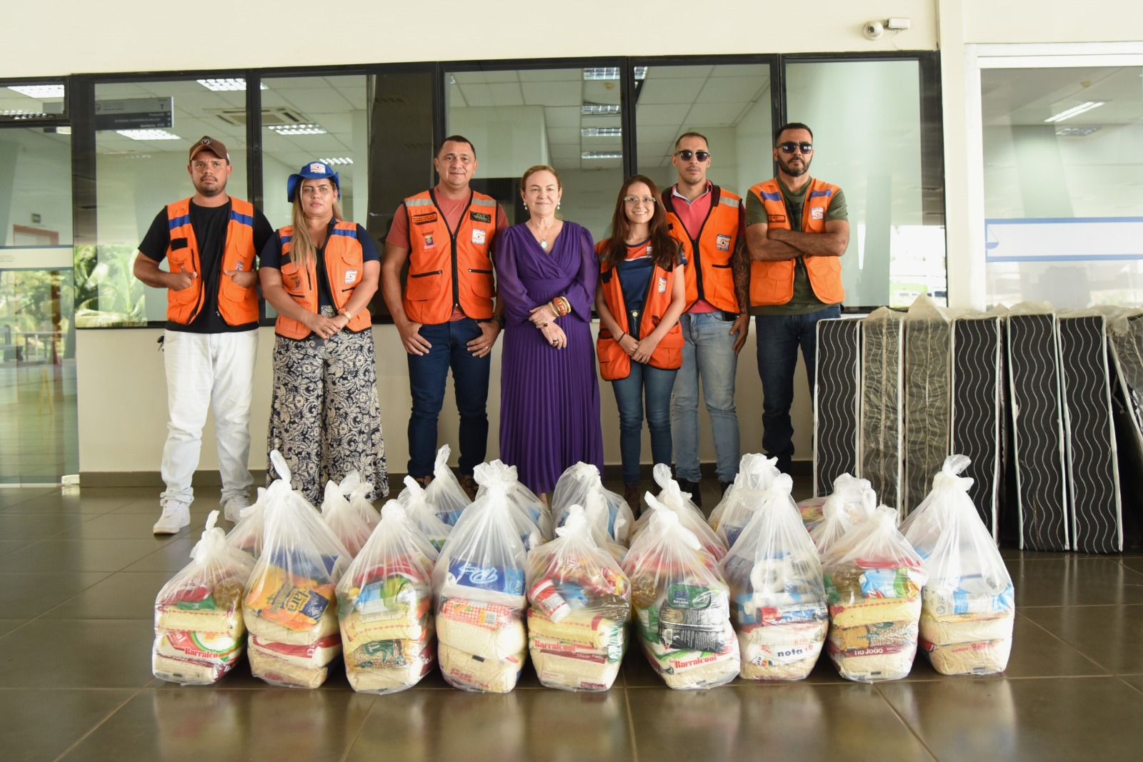 Foto da desembargadora-presidente do Tribunal de Justiça do Acre, Regina Ferrari, com a equipe da Defesa Civil de Rio Branco. Na imagem, no canto direito, há sete colchões de solteiro. À frente dos fotografados, há 26 cestas básicas.