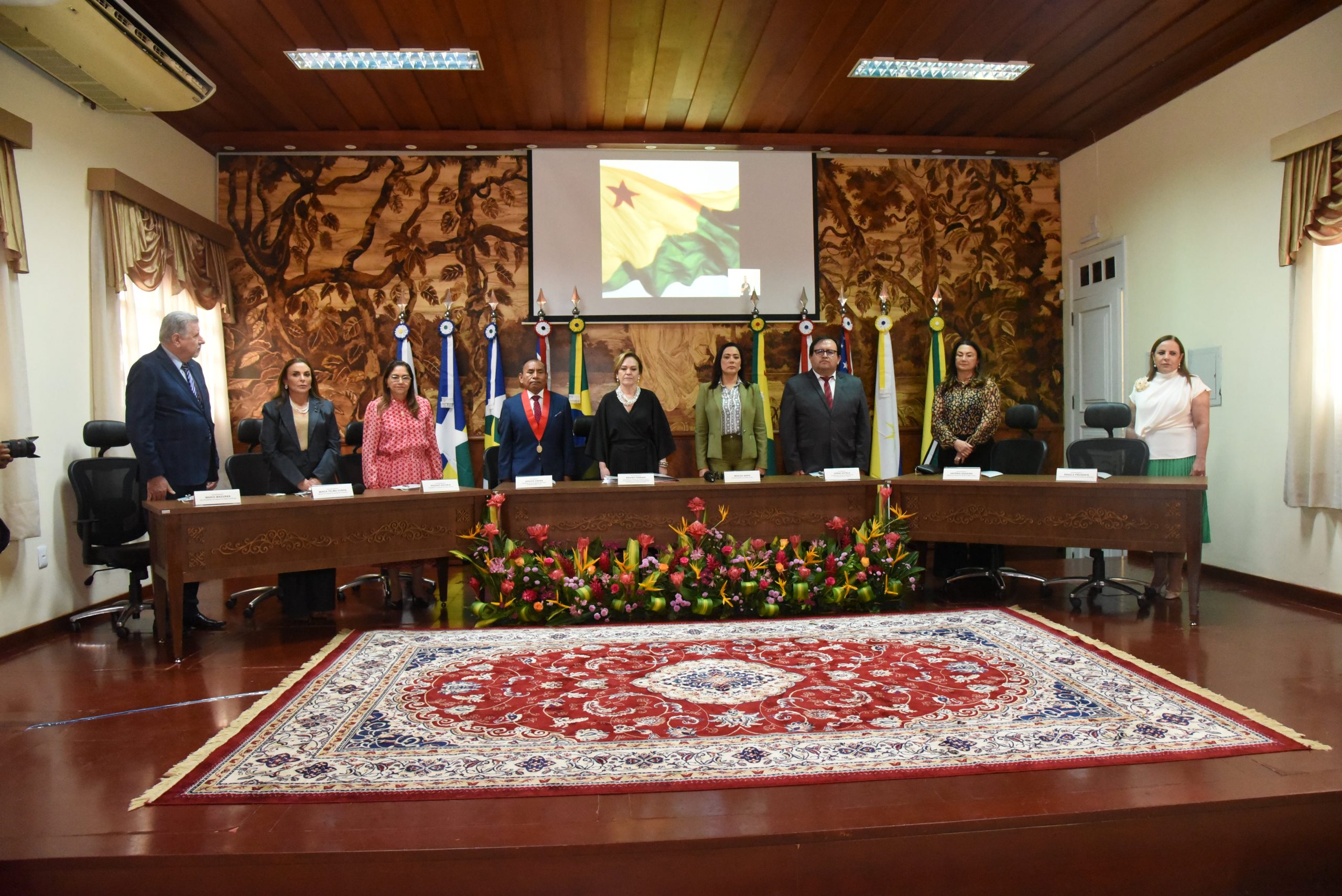 Imagem feita no Plenário do Palácio da Justiça, localizado na rua Benjamin Constant, 277, Rio Branco, Acre, onde a presidente do Tribunal de Justiça do Acre, Regina Ferrari recebe presidentes dos tribunais de justiça da Amazônia Legal, são eles: Acre, Pará, Mato Grosso, Amazonas, Tocantins e Amapá. O presidente da Corte Superior de Justiça de madre de Dios, do Peru, juiz superior Adolfo Cayra, e o presidente do Tribunal Departamental de Justiça de Pando, na Bolívia, juiz superior Jorge Sotelo, foram os convidados internacionais. Presidente do TJAC destaca importância da cooperação durante I Encontro de Tribunais de Justiça da Amazônia Legal Os representantes dos tribunais assinaram a Carta de Cooperação afirmando o compromisso de fortalecer o constante diálogo e a cooperação institucional Destacando sobre colaboração entre os tribunais na identificação de desafios comuns, a busca por soluções mais eficientes e consistentes em prol dos usuários da Justiça, a presidente do Tribunal de Justiça do Estado do Acre (TJAC), desembargadora Regina Ferrari, abriu o I Encontro de Tribunais de Justiça da Amazônia Legal. Com a temática ‘O Poder Judiciário na Amazônia: diálogos e cooperação para o bem servir’, o evento ocorre no Palácio da Justiça e reúne representantes dos tribunais dos estados do Acre, Pará, Mato Grosso, Amazonas, Tocantins e Amapá. O presidente da Corte Superior de Justiça de madre de Dios, do Peru, juiz superior Adolfo Cayra, e o presidente do Tribunal Departamental de Justiça de Pando, na Bolívia, juiz superior Jorge Sotelo, foram os convidados internacionais. “Hoje é o I Encontro dos Tribunais de Justiça da Amazônia Legal. É um marco importante, um marco histórico, onde nós vamos congregar boas práticas e criarmos vários diálogos sobre uma cooperação, construindo pautas que possam auxiliar na edificação do Objetivo 16 da Agenda 2030, da ONU, que emana para nós que sejamos responsáveis por instituições eficazes, paz e justiça”, disse a presidente do TJAC que também é vice-presidente do Conselho de Presidentes dos Tribunais de Justiça do Brasil (Consepre). Pela manhã, durante a abertura, que foi bastante prestigiada por servidoras, servidores, magistradas, magistrados, autoridades locais do sistema de justiça e demais operadores do Direito, todos os representantes dos tribunais compartilharam suas expectativas para o evento abordando questões relacionadas aos serviços jurisdicionais e parabenizaram o TJAC pela iniciativa em reunir os tribunais para trocar experiências, aprender com os sucessos e desafios de outros tribunais e aprimorar o sistema judiciário como um todo. O vice-presidente do Tribunal de Justiça do Amapá, desembargador Mário Mazurek, por exemplo, destacou sobre a peculiaridade dos estados, onde o evento é essencial para uma apreciação mais profunda e uma compreensão mais abrangente do sistema de cada tribunal. A presidente do Tribunal de Justiça do Pará, desembargadora Nazaré Gouveia, salientou sobre estreitar as conquistas de cada tribunal, e o presidente da Corte Superior de Justiça de Madre de Dios, no Peru, juiz superior Adolfo Cayra, ressaltou que os encontros, como o de hoje, geram um impacto poderoso no compromisso da judicatura. Representando o Governo do Acre, que é um dos apoiadores do evento, a vice-governadora Mailza Assis destacou que Tribunal de Justiça do Acre está de parabéns e tem se destacado em práticas de Justiça Restaurativa através de projetos e ações. “Nossa tarefa hoje é discutir as situações dos tribunais de Justiça da Amazônia e pensar no fortalecimento de programas e projetos que leve a Justiça mais próximo da população”, destacou. Cooperação Judiciária Seguindo a programação, na parte da tarde, os participantes concentraram-se na Sala de Reunião do Palácio da Justiça para apresentar projetos desenvolvidos em seus tribunais. Na abertura, o corregedor-geral da Justiça do Acre, desembargador Samoel Evangelista, enfatizou que o momento de compartilhar as boas práticas promove a transparência, a melhoria contínua que são elementos essenciais para a confiança na justiça. “Esses encontros também oferecem um espaço para discutir questões complexas e atuais que afetam o sistema judiciário, permitindo a busca por soluções colaborativas e alinhadas com as necessidades da sociedade”, disse o corregedor que apresentou alguns projetos executados pelo órgão onde três foram premiados nacionalmente. Carta do Encontro Tráfico ilegal de madeira, tráfico humano, guerra entre facções, pesca e caça ilegal, migração, o baixo índice de crianças matriculadas na Amazônia foram alguns pontos discutidos entre os magistrados. Ao encerrar o evento, os presidentes e representantes dos tribunais assinaram a carta firmando o compromisso de fortalecer o constante diálogo e a cooperação institucional entre os tribunais de Justiça da Amazônia Legal para a superação de desafios comuns, com foco no desenvolvimento sustentável, proteção ao meio ambiente, integração dos povos amazônicos e a inclusão social. Entre os compromissos, os participantes garantiram compartilhar boas práticas, projetos e tecnologias para melhorar a prestação jurisdicional, reafirmaram a necessidade de observância das peculiaridades geográficas, econômicas e sociais, sobretudo na interlocução com o Conselho Nacional de Justiça no esforço de construir uma política de Estado para o Poder Judiciário nacional equalizada de acordo com as realidades regionais. Propor a continuidade de encontros, com periodicidade mínima de dois eventos por ano, afim de consolidador e aperfeiçoar a rede de cooperação entre as instituições, além de preservarem a harmonia institucional e a deliberação democrática para atendimento das demandas da sociedade.